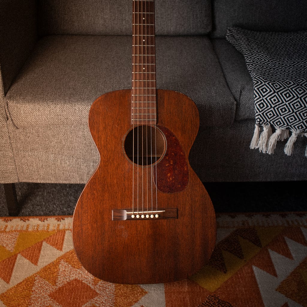 vintage martin guitar in front of a grey tweed sofa